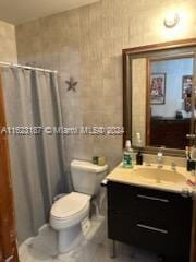 bathroom with vanity, tile walls, curtained shower, and toilet