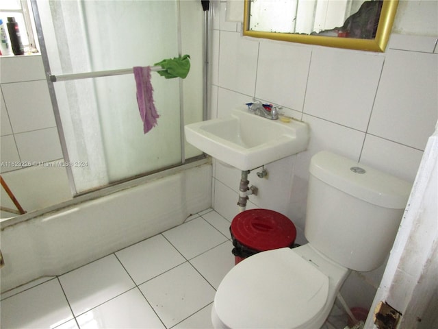 full bathroom with tile walls, sink, bath / shower combo with glass door, and toilet