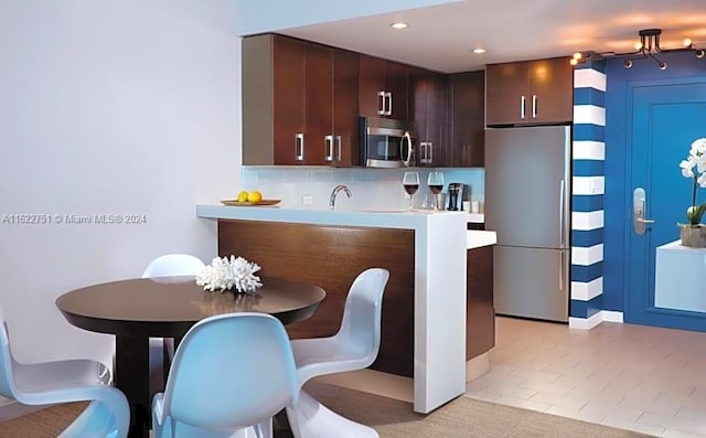 kitchen with light tile patterned flooring, dark brown cabinets, tasteful backsplash, appliances with stainless steel finishes, and kitchen peninsula