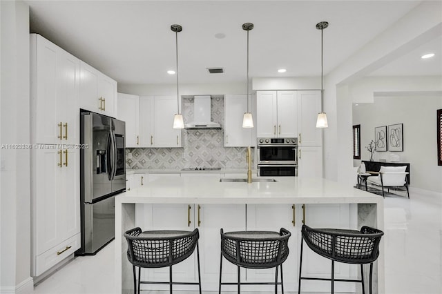 kitchen with appliances with stainless steel finishes, pendant lighting, white cabinets, and wall chimney exhaust hood