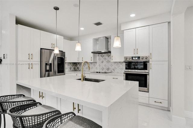 kitchen with pendant lighting, white cabinetry, sink, stainless steel appliances, and wall chimney exhaust hood