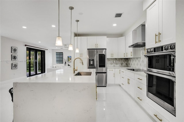 kitchen featuring sink, white cabinetry, decorative light fixtures, stainless steel appliances, and wall chimney range hood