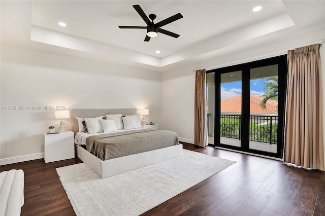 bedroom with dark wood-type flooring, ceiling fan, a tray ceiling, and access to outside