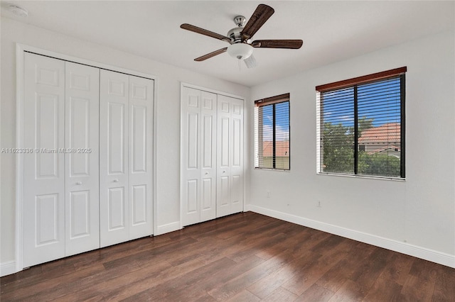 unfurnished bedroom featuring two closets, dark wood-type flooring, and ceiling fan