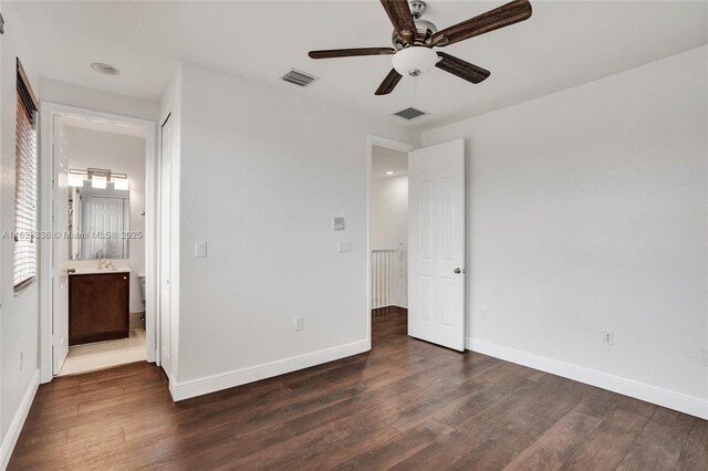 unfurnished bedroom featuring ensuite bathroom, dark wood-type flooring, sink, and ceiling fan