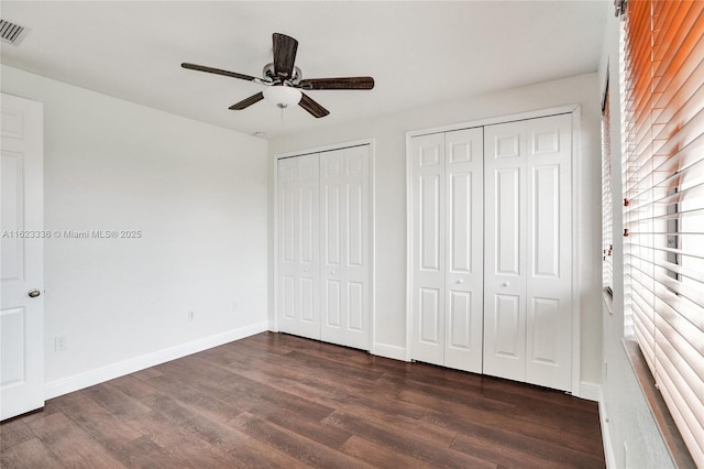 unfurnished bedroom with dark wood-type flooring, two closets, and ceiling fan