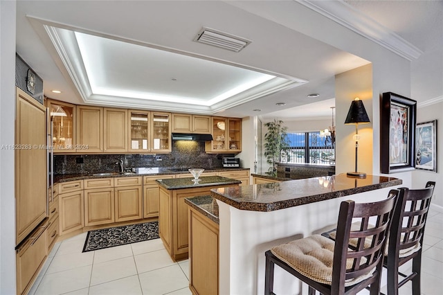 kitchen with backsplash, a breakfast bar area, a raised ceiling, and crown molding