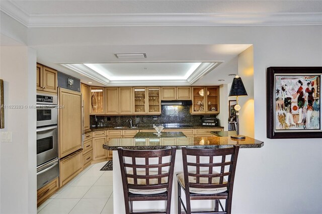 kitchen featuring a tray ceiling, tasteful backsplash, ornamental molding, and double oven