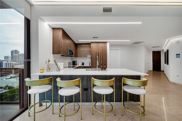 kitchen featuring a kitchen bar, tasteful backsplash, sink, kitchen peninsula, and light tile patterned floors