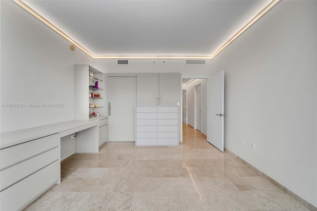 unfurnished bedroom with light tile patterned flooring, built in desk, a closet, and a tray ceiling