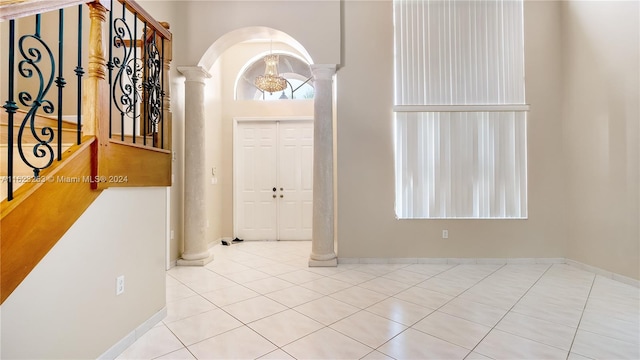 tiled entryway featuring a towering ceiling, a notable chandelier, and decorative columns