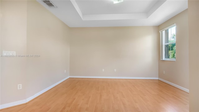 unfurnished room featuring a tray ceiling and light hardwood / wood-style floors