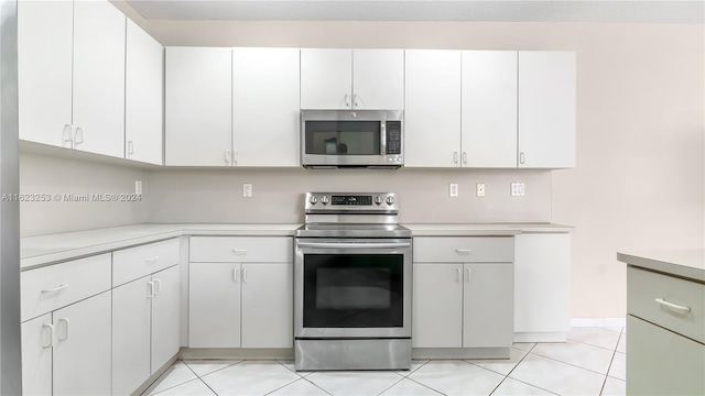 kitchen with appliances with stainless steel finishes, light tile patterned floors, and white cabinetry