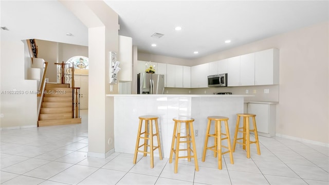 kitchen with appliances with stainless steel finishes, light tile patterned floors, a kitchen breakfast bar, kitchen peninsula, and white cabinets