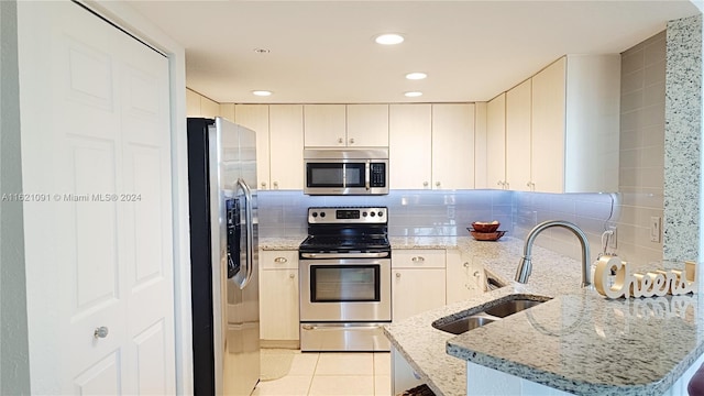 kitchen with sink, light tile patterned flooring, light stone counters, kitchen peninsula, and stainless steel appliances