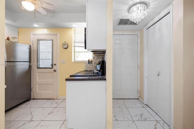 kitchen featuring stainless steel refrigerator, light tile patterned floors, ceiling fan with notable chandelier, and tasteful backsplash