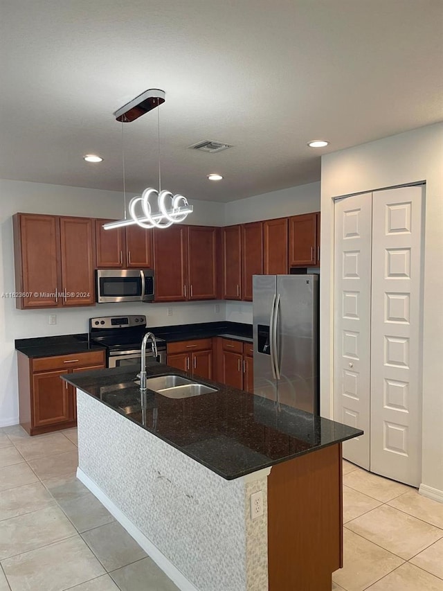 kitchen with a kitchen island with sink, hanging light fixtures, stainless steel appliances, dark stone countertops, and sink