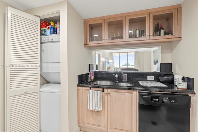 kitchen featuring dark stone countertops, dishwasher, sink, and stacked washing maching and dryer