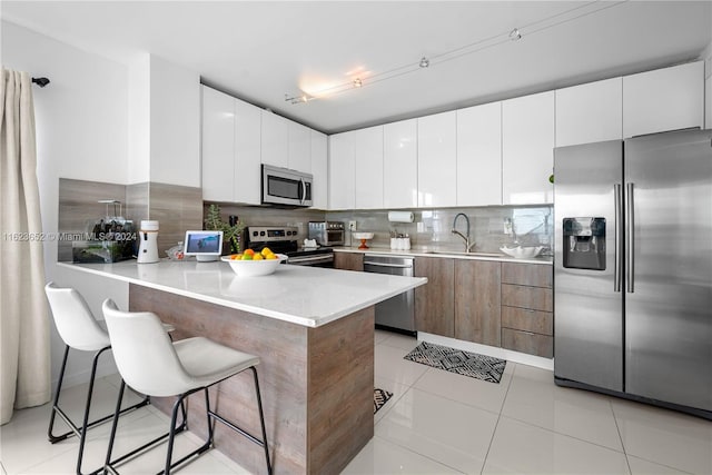 kitchen featuring stainless steel appliances, white cabinets, a sink, and a breakfast bar area