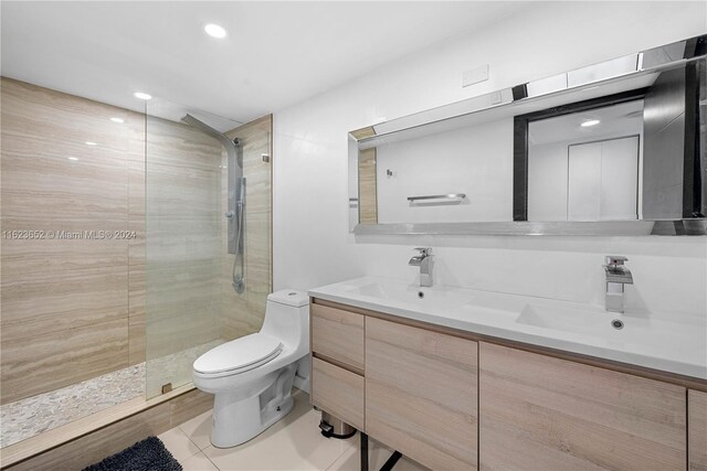 bathroom with a shower with door, vanity, tile patterned floors, and toilet