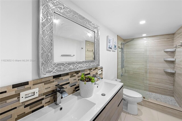 bathroom with tile patterned flooring, double sink vanity, tasteful backsplash, toilet, and a tile shower