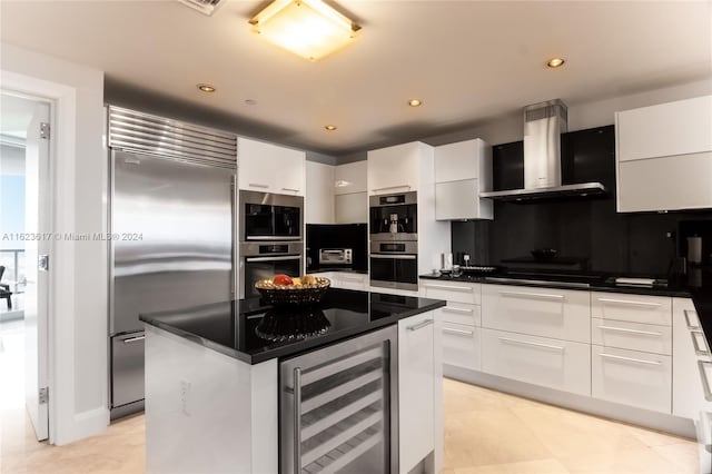 kitchen featuring white cabinetry, a center island, beverage cooler, stainless steel appliances, and wall chimney exhaust hood