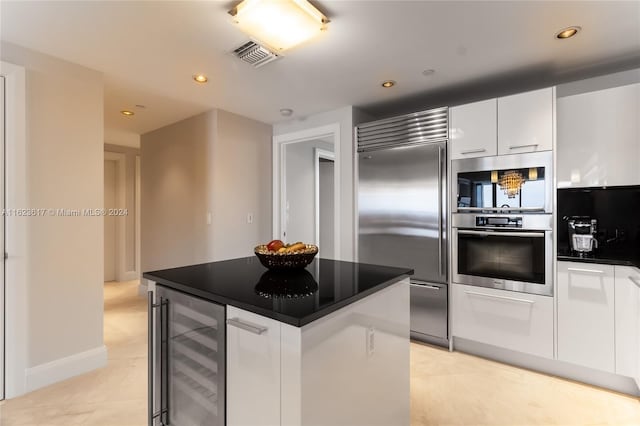 kitchen featuring appliances with stainless steel finishes, light tile patterned floors, a center island, white cabinetry, and beverage cooler