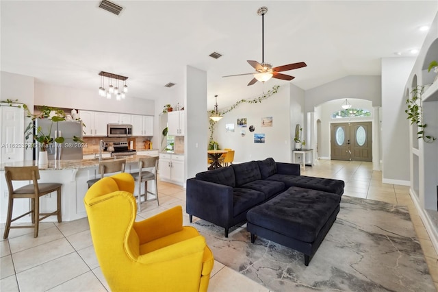 living room featuring ceiling fan with notable chandelier, light tile patterned floors, sink, and vaulted ceiling