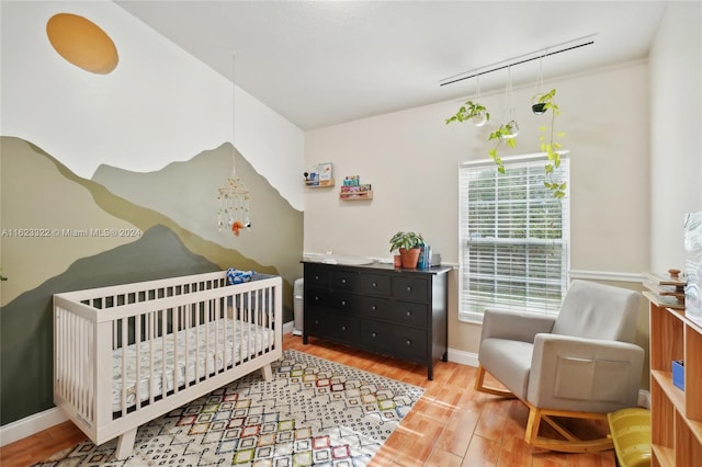 bedroom with hardwood / wood-style floors, rail lighting, and a nursery area