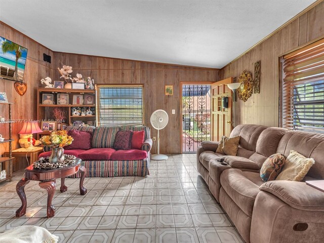 living room with plenty of natural light, wood walls, tile patterned flooring, and lofted ceiling