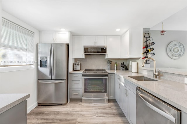 kitchen with sink, white cabinetry, stainless steel appliances, light stone countertops, and light hardwood / wood-style floors