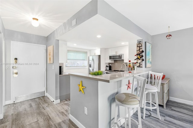 kitchen featuring appliances with stainless steel finishes, white cabinetry, a kitchen breakfast bar, kitchen peninsula, and light hardwood / wood-style flooring