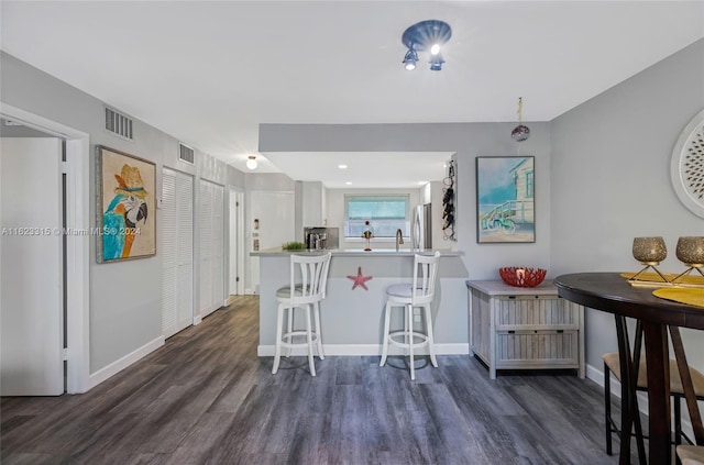 kitchen with a breakfast bar area, white cabinetry, stainless steel refrigerator, dark hardwood / wood-style floors, and kitchen peninsula