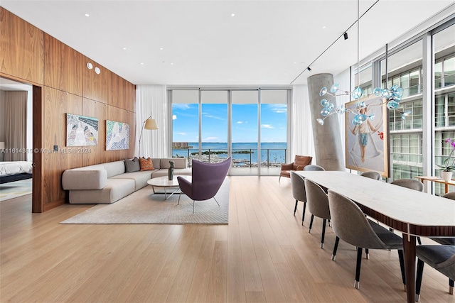 living room with light hardwood / wood-style floors, a wall of windows, a water view, and wood walls