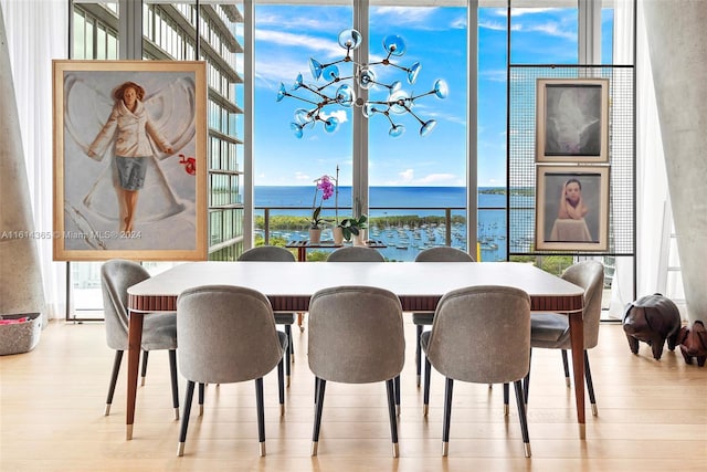 dining space featuring floor to ceiling windows, light hardwood / wood-style floors, a chandelier, and a water view