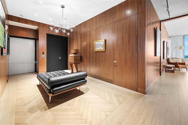 hallway featuring rail lighting, wood walls, an inviting chandelier, and light parquet flooring