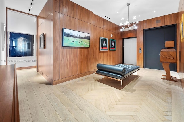 interior space featuring elevator, an inviting chandelier, wood walls, and light parquet flooring