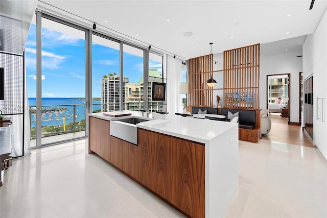 kitchen featuring pendant lighting, a water view, a center island with sink, a wall of windows, and sink