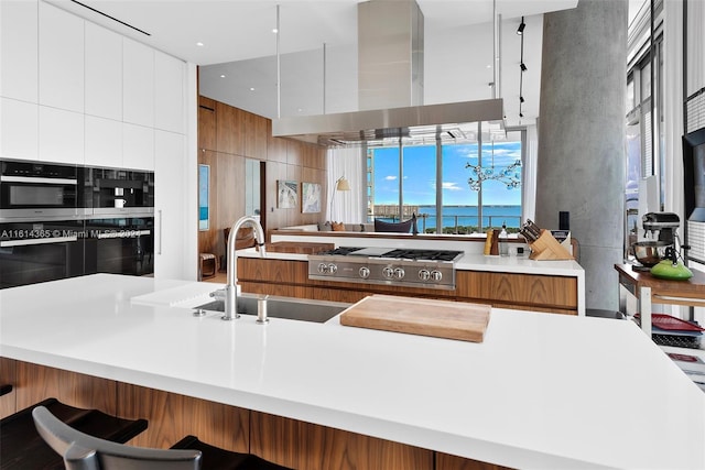 kitchen with white cabinets, stainless steel gas stovetop, wall chimney range hood, and sink