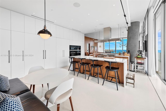 kitchen with a spacious island, wall chimney range hood, pendant lighting, and a kitchen bar