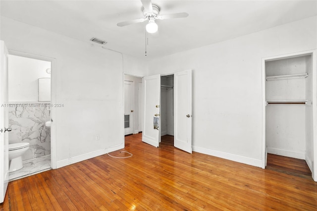 unfurnished bedroom with ceiling fan, hardwood / wood-style flooring, connected bathroom, and two closets