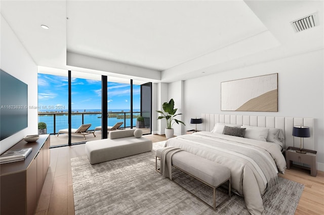 bedroom with a wall of windows, access to exterior, a raised ceiling, a water view, and light hardwood / wood-style flooring