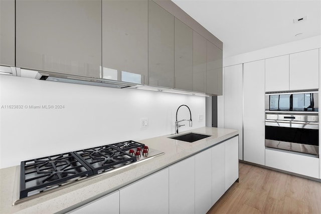 kitchen with sink, light hardwood / wood-style flooring, white cabinetry, stainless steel appliances, and light stone countertops