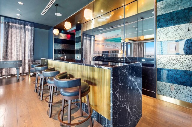 bar with dark stone countertops, hanging light fixtures, and light wood-type flooring