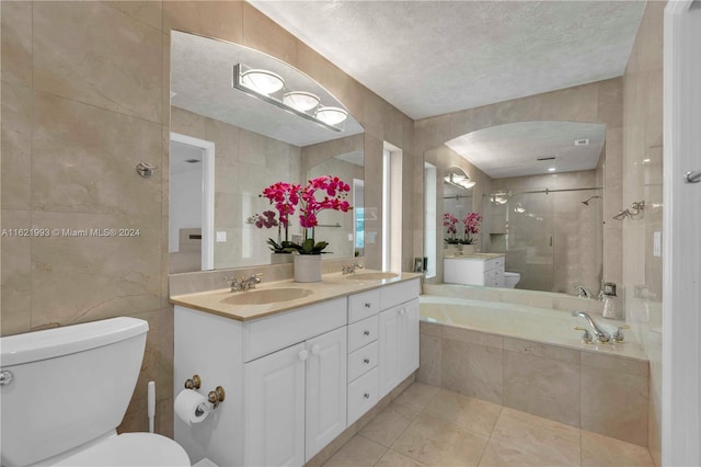 bathroom featuring double sink vanity, tile walls, toilet, a textured ceiling, and tile patterned flooring