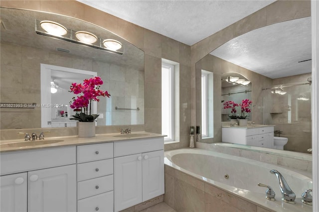 bathroom featuring ceiling fan, dual bowl vanity, toilet, a textured ceiling, and a relaxing tiled tub