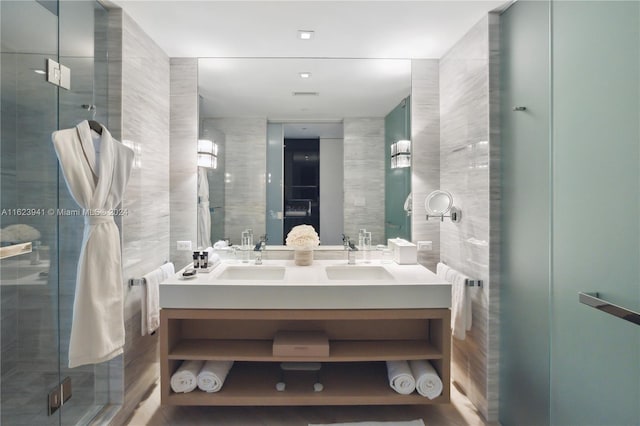 bathroom with a shower with shower door, double sink vanity, and tile walls