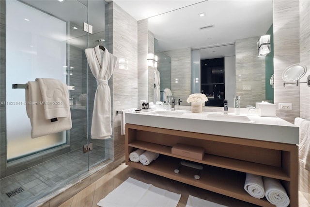 bathroom with a shower with door, tile walls, dual bowl vanity, and tile patterned flooring