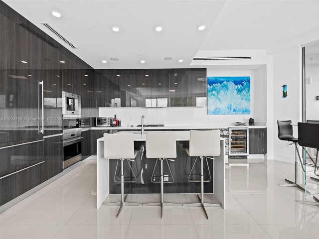 kitchen featuring a center island with sink, beverage cooler, stainless steel oven, and a kitchen bar