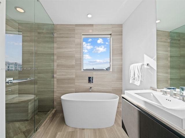 bathroom with shower with separate bathtub, tile walls, and vanity